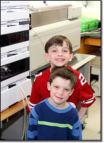 Connor (back) and Kellen Brown standing beside the machine that screened their bloodspots years ago – the very machine that saved their lives.