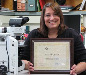 Michele Smith holding her ASCT award in her office