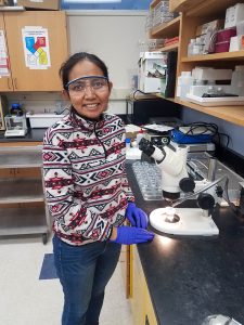 Nina Desianti stands in front of a lab bench with a microscope.